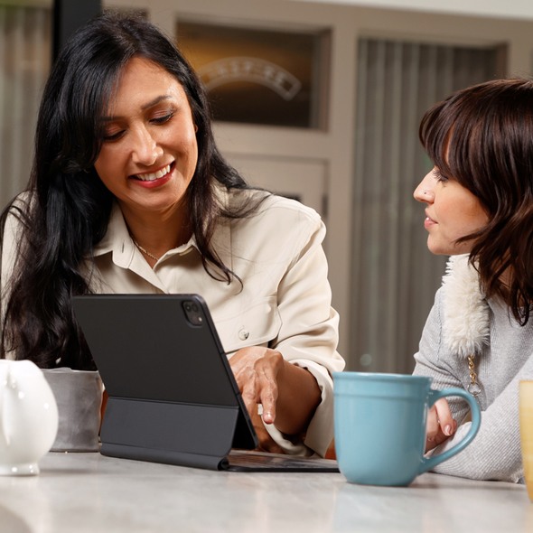 One woman introduces another to TruStage financial solutions on her notebook while having a cup of coffee
