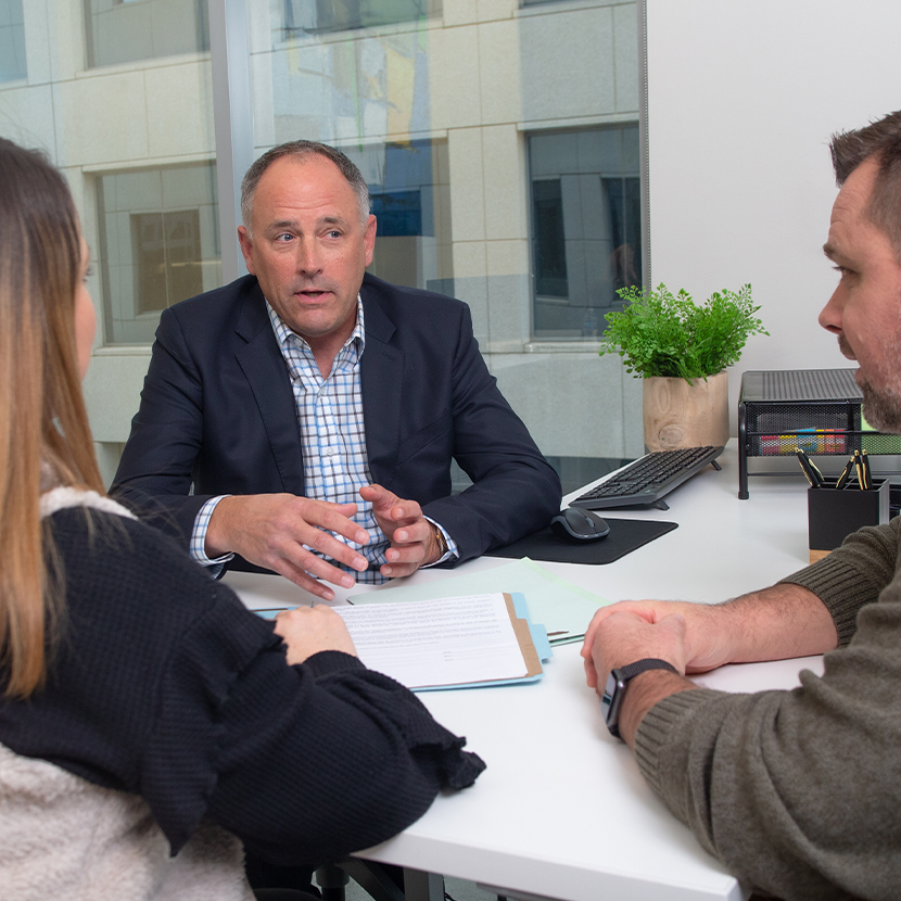 Three people sitting at a table, in an office setting, talking.