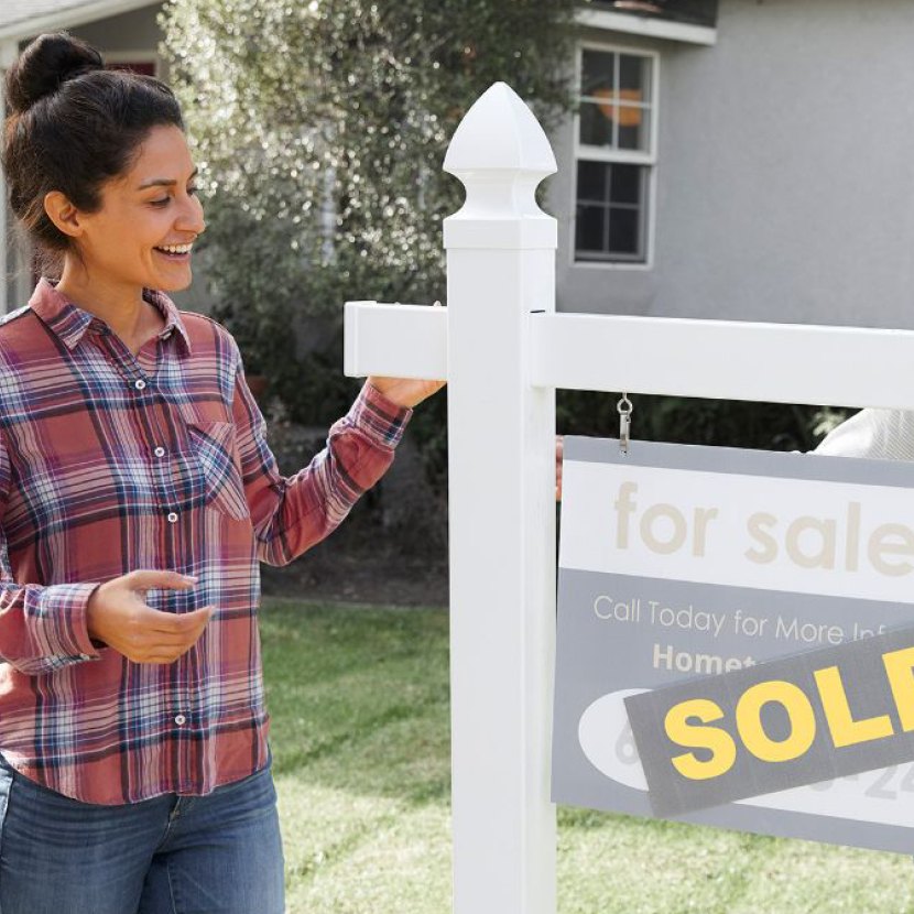 Woman standing next to a "for sale" sign